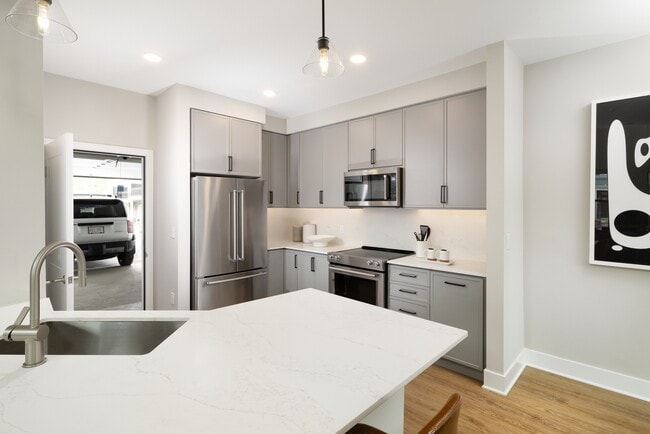 Signature Collection kitchen with stainless steel appliances, white quartz countertop, grey cabinetry, white quartz backsplash, hard surface flooring, and attached garage - Avalon Wayne Apartments