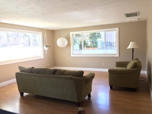 Living room with large windows and tree views. Couches not included. - 1152 NE Viking Ct