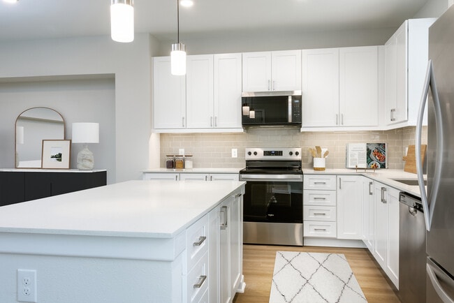 Finish Package I townhome kitchen with stainless steel appliances, white cabinetry, grey tile backsplash, white quartz countertops, and hard surface flooring