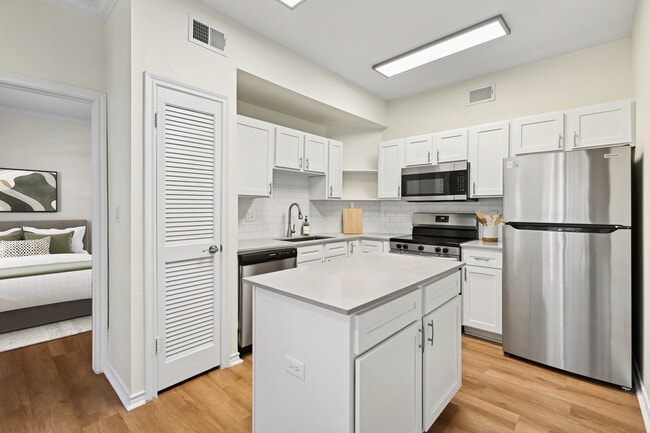 Renovated Package I kitchen with stainless steel appliances, white cabinetry, white tile backsplash, grey quartz countertops, and hard surface flooring - eaves North Dallas