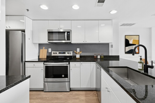 Cocina renovada del Paquete I con gabinetes blancos, encimeras de granito negro, electrodomésticos de acero inoxidable y pisos de superficie dura.