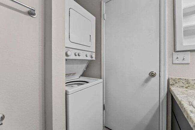 In-unit stacked washer and dryer inside a closet nook adjacent to a bathroom with granite countertop vanity
