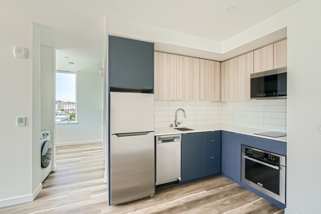 Experience the open layout of this modern kitchen and living room at Anker Ballard, featuring hardwood floors and a stunning city view.