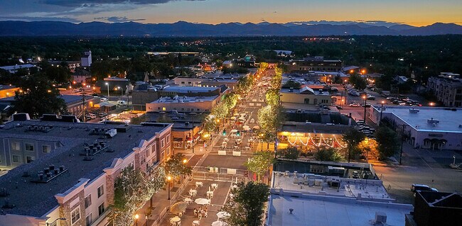 Enchanting evening aerial view of a lively city street lined with twinkling lights, bustling cafes, and picturesque mountain backdrop.