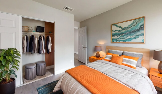 Bright and inviting bedroom with a modern design, featuring a cozy bed with orange accents, an open closet neatly organized, and stylish decor.