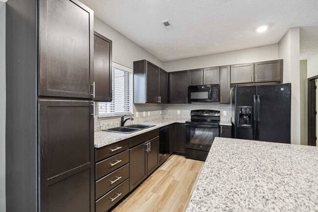 Cook and create with ease in this stylish kitchen featuring granite countertops, black appliances, and rich dark cabinetry with natural light from the window above the sink.