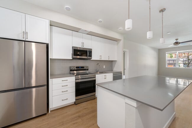Finish Package I Kitchen with white cabinetry, grey quartz countertops, grey tile backsplash, stainless steel appliances, and hard-surface vinyl plank flooring