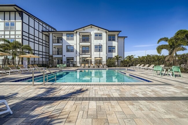 Luxurious apartment complex with a pristine outdoor pool area, surrounded by stylish loungers and palm trees under a clear blue sky.