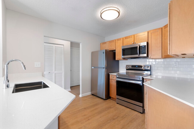 Renovated Package I kitchen with stainless steel appliances, white quartz countertops, maple cabinetry, white tile backsplash, and hard surface flooring - Avalon Burlington