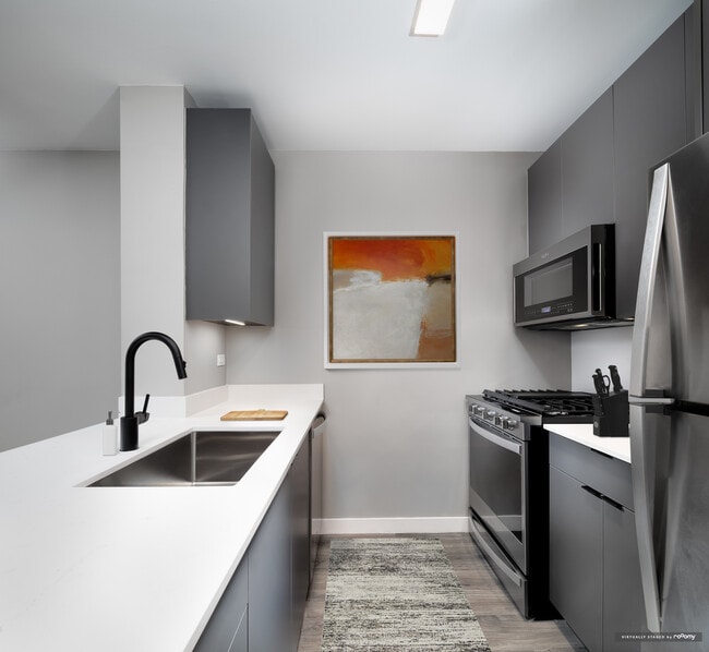 Renovated Package II kitchen with white quartz countertop and backsplash, upgraded stainless steel appliances, upgraded black hardware, and upgraded lighting - Avalon Midtown West Apartments