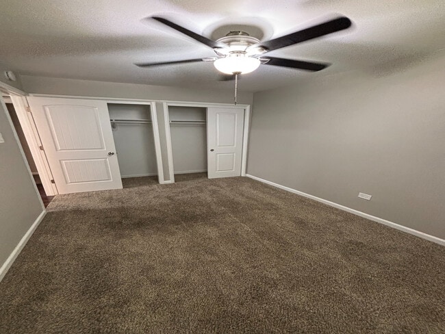 Bright bedroom featuring soft carpet, a ceiling fan, and double closet doors, offering comfort and ample storage. - Redwood Apartments