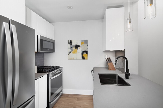 Renovated Package I kitchen with stainless steel appliances, white cabinetry, grey tile backsplash, grey quartz countertops, and hard-surface flooring (Representative Imagery) - Avalon Riverview