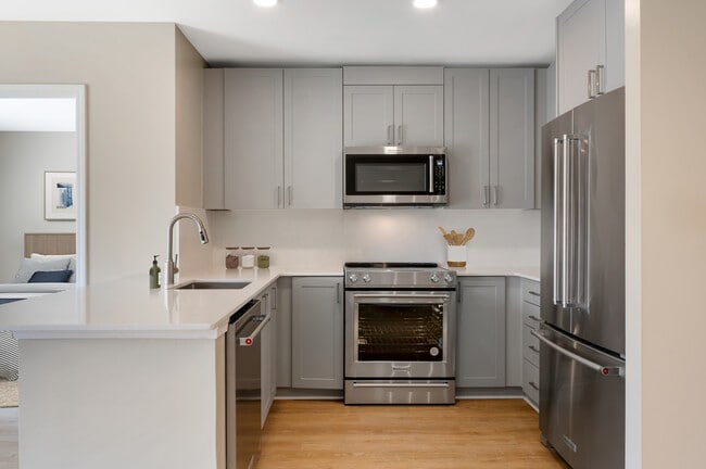 Signature Collection kitchen with grey cabinetry, white marbled quartz countertops and backsplash, stainless steel appliances, and hard surface flooring - Avalon Clarendon Apartments