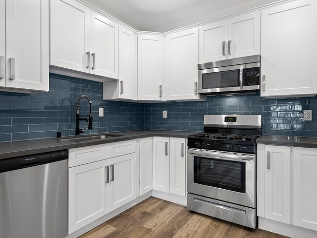 Blue tiled kitchen with stainless steel fridge, oven, and microwave.
