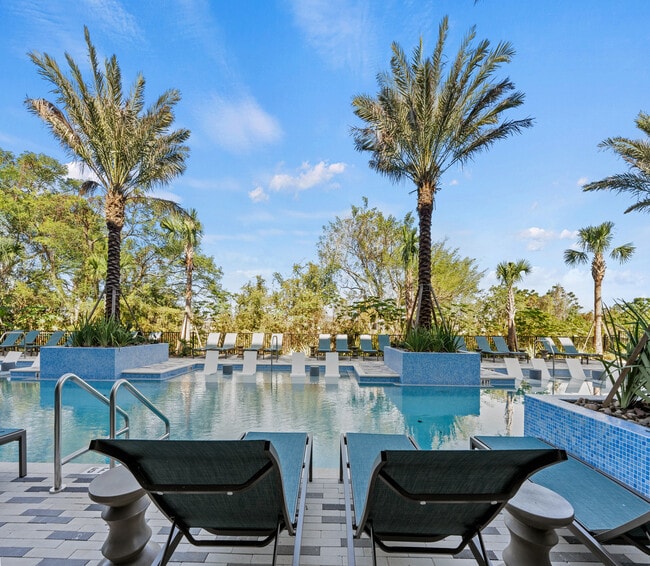 Luxurious pool area with elegant lounge chairs and towering palm trees, set against a stunning blue sky backdrop. - Elan Crown Point