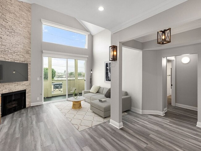 Hardwood floored living room with view of stone accent wall, fireplace, and high third-floor ceilings.