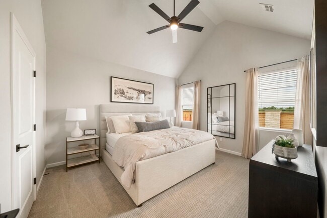 Primary bedroom with vaulted ceiling, ceiling fan, plush carpet, and large windows with neutral curtains