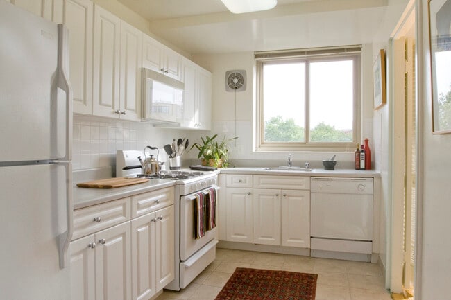 Kitchen with white cabinetry, white countertops, white appliances, tile backsplash and tile flooring - Avalon The Albemarle Apartments