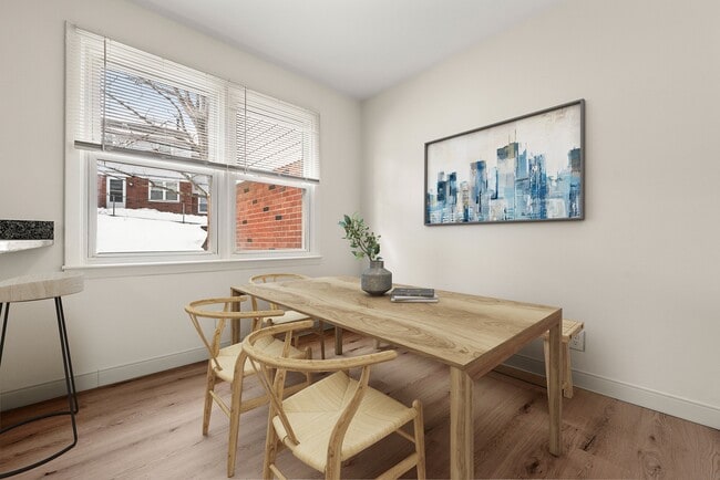 Bright and modern dining area with large windows, stylish wooden table and chairs, cityscape artwork, and sleek light wood flooring.