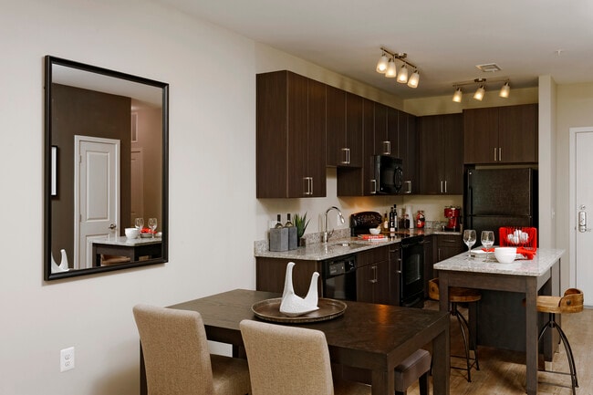 Contemporary dining area and kitchen with espresso cabinetry, grey granite countertops, black appliances, and hard surface flooring