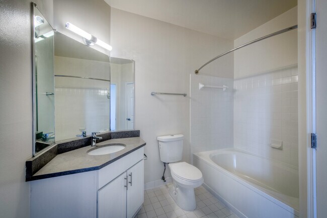 Renovated Package II bathroom with white cabinetry, grey quartz countertop, and hard surface flooring - Avalon Reston Landing