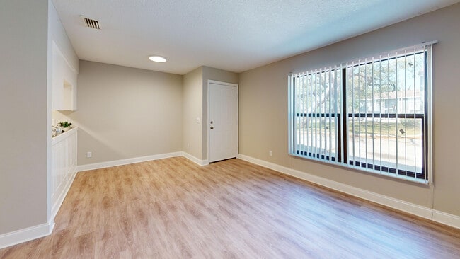Bright and inviting living room with large windows and elegant wood flooring, ideal for relaxation and entertaining. - Chateau of Tampa