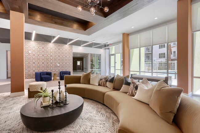 Kick back in style. The main lounge anchors the Garrett Uptown clubhouse with a statement curved sectional, bold accent tile, and natural light pouring in from the pool courtyard.