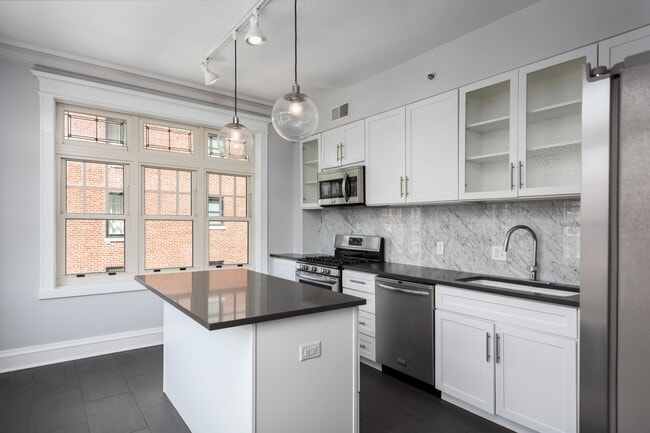 York House designer kitchen with gas stove, quartz countertops, stainless steel appliances, marble kitchen backsplash, and slate tile floor.