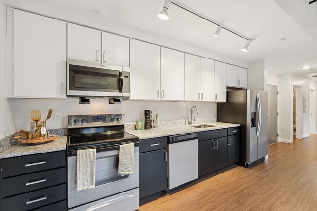 Cocina moderna de apartamento con electrodomésticos de acero inoxidable, gabinetes blancos y encimeras de granito.