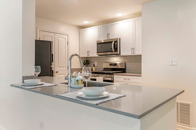 Renovated Package I kitchen with white cabinetry, grey quartz countertops, grey tile backsplash, stainless steel appliances, and hard surface plank flooring - Avalon at The Pinehills Apartments