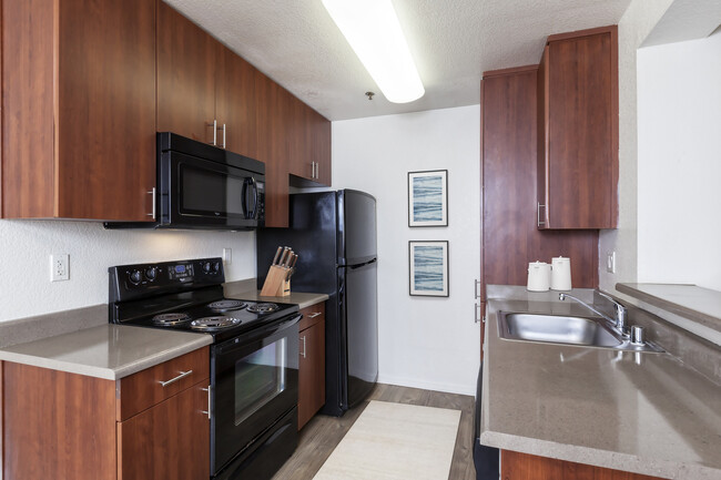 Kitchen with cherry cabinetry, light grey countertop, black appliances and hard surface flooring - eaves Pleasanton Apartments