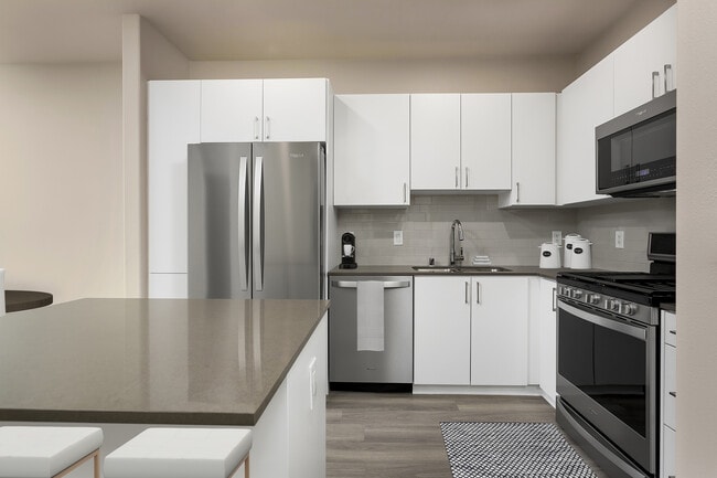 Renovated Package I kitchen with quartz countertops, white cabinetry, stainless steel appliances, hard surface vinyl plank flooring, and tile backsplash