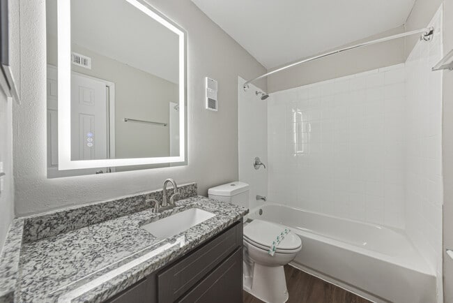 Baño moderno con tocador de granito y combinación de bañera y ducha. - Magnolia Apartments