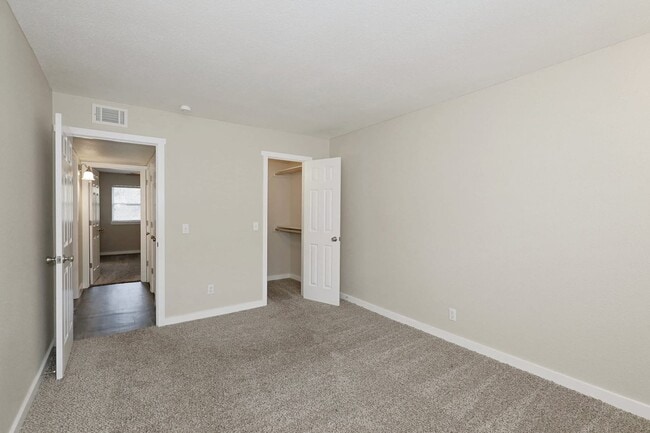 Bedroom with carpet flooring, neutral walls, open closet, and doorway leading to hallway with wood style flooring