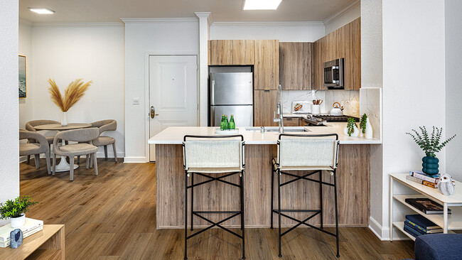 Gourmet kitchen and dining area with stainless steel appliances, quartz countertops and wood-style flooring. - Griffis South Bay Apartments