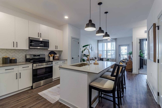 Cook and gather in the open-concept kitchen of the A1 floor plan, featuring a quartz island with seating, stainless steel appliances, and a herringbone tile backsplash. - Garrett Gateway