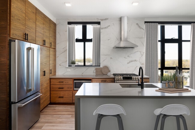 Kitchen with wood cabinetry, grey quartz countertops, marble backsplash, stainless steel appliances, and hard surface flooring - Avalon Hawk Apartments