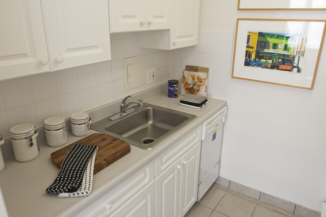 Cocina de apartamento tipo estudio con un amplio lavabo de acero inoxidable, lavaplatos y gabinetes de color blanco - The Statesman Apartamentos