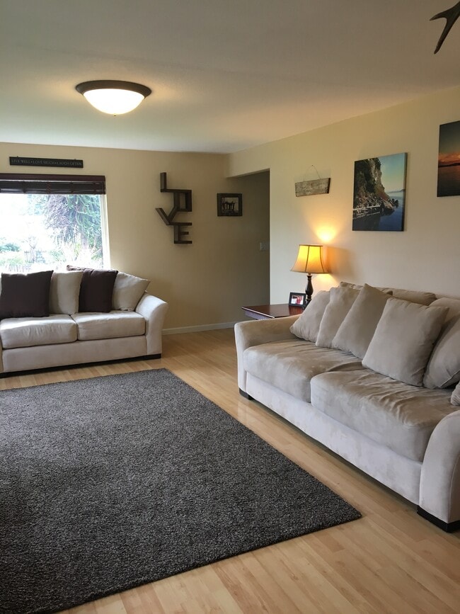 Large living room with lots of windows, wood burning fireplace. Light wood laminate floors.
