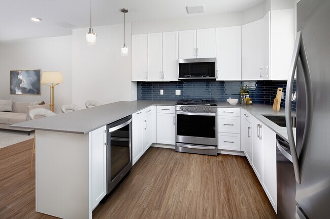 Phase II Renovated Package I townhome kitchen with stainless steel appliances, grey quartz countertops, white cabinetry, grey tile backsplash, and hard surface flooring