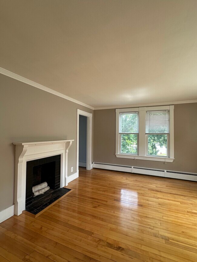 Bright, sunlit living room with decorative wood-burning fireplace and hardwood floors - 363 Concord Rd Unit 2