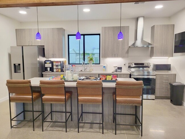 Modern clubhouse kitchen with wood cabinets, snack bar, pendant lights, and four cushioned bar stools with backs