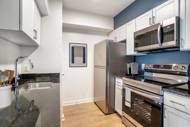 Renovated Package II kitchen with stainless steel appliances, white shaker cabinetry, dark speckled granite countertops, and hard surface flooring