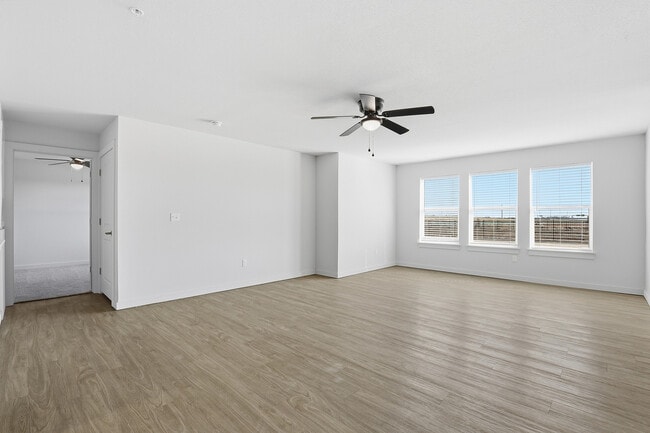 Sala de estar amplia y luminosa con elegantes pisos de madera, grandes ventanales que ofrecen luz natural y un moderno ventilador de techo. - Oaks at Mustang