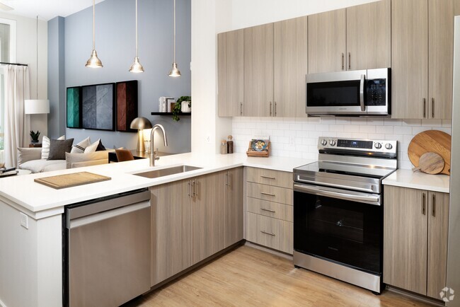 Modern kitchen with oak cabinetry, white tile backsplash, white quartz countertops, stainless steel appliances, and pendant lighting - Avalon Durham Rental