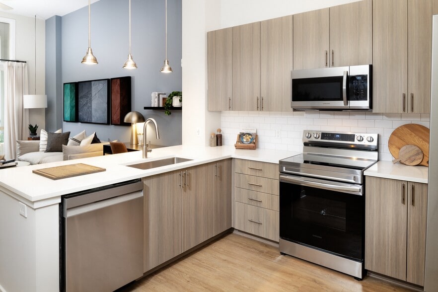 Modern kitchen with oak cabinetry, white tile backsplash, white quartz countertops, stainless steel appliances, and pendant lighting