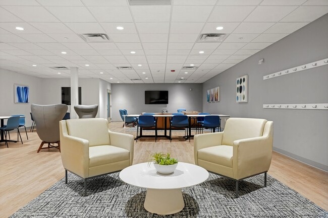 Bright and contemporary shared space featuring plush seating, modern decor, and a versatile meeting area with stylish blue chairs.