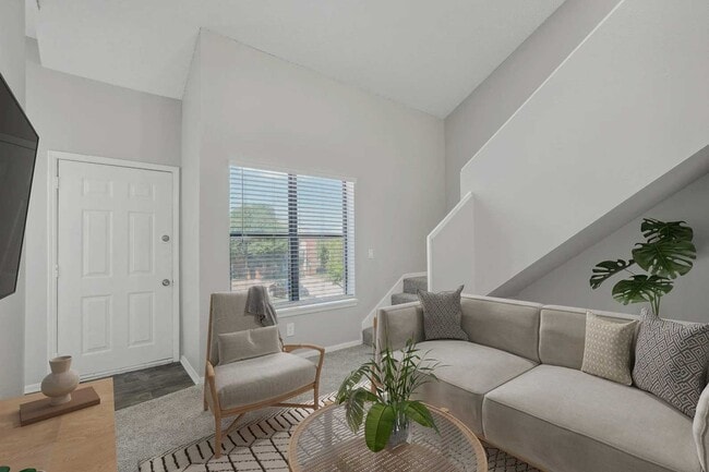 Bright living room with vaulted ceiling, gray sectional sofa, accent chair, indoor plants, staircase, and front door