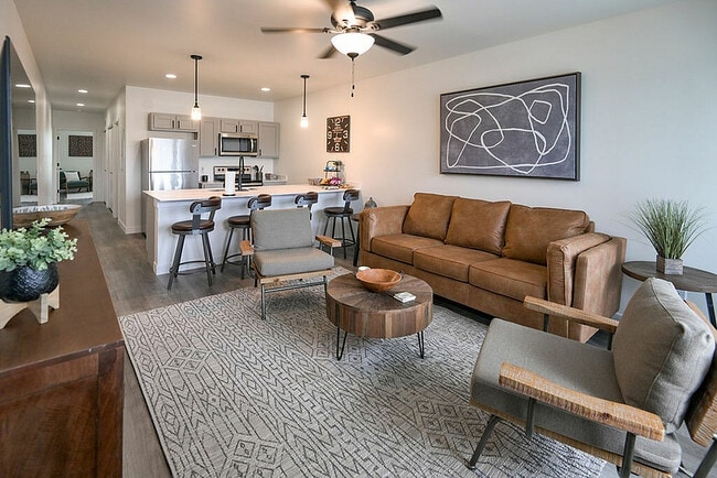 Modern open-plan living space with cozy leather sofa, sleek kitchen, and stylish bar seating, perfect for entertaining. - Highland Park Apartments