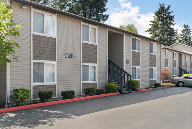 Appealing apartment building with carport parking, landscaped greenery, and a clear blue sky backdrop.